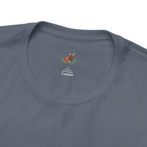 May include: A dark blue t-shirt with a white tag featuring a fox and a moose illustration. The tag also includes the text "100% Cotton Made in Bangladesh" and a size L label.
