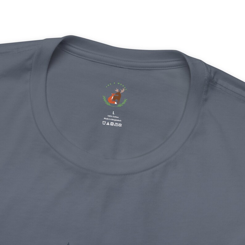 May include: A dark blue t-shirt with a white tag featuring a fox and a moose illustration. The tag also includes the text "100% Cotton Made in Bangladesh" and a size L label.