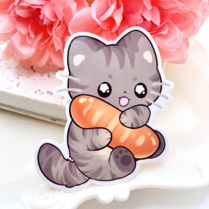Puede incluir: Una pegatina con un gato de dibujos animados con rayas grises y blancas, abrazando una barra de pan. El gato tiene ojos grandes y una lengua rosa. El fondo incluye flores rosas y una superficie blanca.
