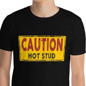 May include: Black t-shirt with a yellow and red sign that says "CAUTION HOT STUD".