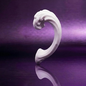 May include: A white, curved, sculptural object with a smooth, matte finish and a wave-like, organic form. The piece features a rounded top that tapers down to a narrower base, creating a C-shaped silhouette with fluid, rippled textures.