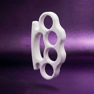May include: A white, solid-coloured knuckle duster featuring four circular finger holes and a smooth, rounded exterior frame. The object is presented in a side-profile view, showcasing its uniform matte finish and curved, ergonomic shape.