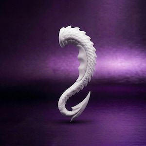 Könnte beinhalten: Ein weißer, geschwungener Ohrschmuck mit einem detaillierten, texturierten Schuppenmuster entlang der gesamten Länge. Das Stück hat ein spitz zulaufendes Ende und einen glatten, konkaven Innenbereich, der sich um den äußeren Rand des Ohrs legt.