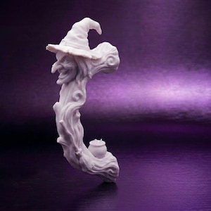 Peut inclure: Une bougie sculptée blanche en forme de sorcière portant un chapeau pointu, avec un long corps texturé et fluide qui se courbe vers le bas. À la base de la figurine, un petit chaudron rond est intégré au design de la bougie.