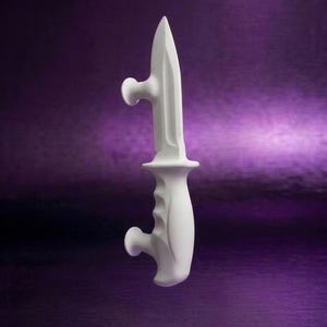Peut inclure: Un objet sculptural blanc mat en forme de couteau tactique avec une lame pointue, une garde centrale et un manche profilé. Le design présente deux petites protubérances circulaires s'étendant depuis la lame et la base du manche.