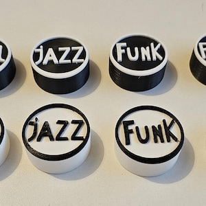 May include: Eight round black and white knobs with the words "Soul", "Jazz", "Funk", and "Rock" printed in white on a black background. The knobs are arranged in two rows of four.