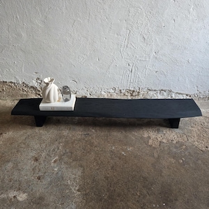 May include: A white ceramic mug with a black handle and the text "But First, Coffee" in a bold, black font. The mug is set against a blurred background, suggesting a cosy setting.