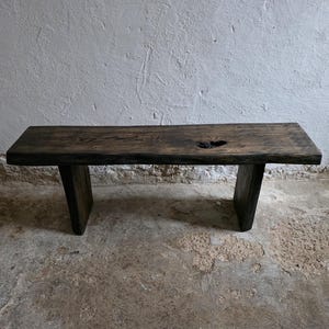 May include: A rustic, dark brown wooden bench with a rectangular top and two sturdy, rectangular legs. The wood has a natural, weathered appearance with a knot detail on the surface. The bench is suitable for indoor or outdoor use.