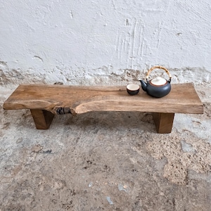May include: A rustic wooden serving tray with a live edge design, supported by two wooden legs. A small, dark blue teapot with a bamboo handle and a matching teacup sit on the tray. The tray is approximately 36 inches long.