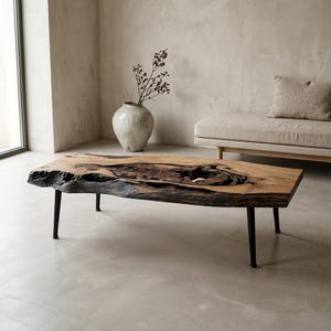May include: A rectangular wooden coffee table with a live edge and dark, black metal legs. The table has a natural wood grain and a unique, organic shape. The table is approximately 122 cm long, 61 cm wide, and 41 cm tall.