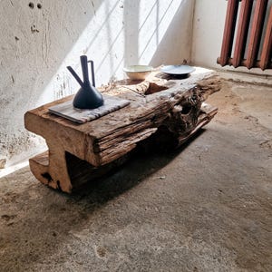 Könnte beinhalten: Ein rustikaler Holz-Couchtisch aus einem großen Baumstamm mit einer natürlichen, rauen Oberfläche. Der Tisch hat eine einzigartige Form mit einer Spalte in der Mitte. Zwei kleine Schalen und ein schwarzer Keramik-Krug stehen auf dem Tisch.