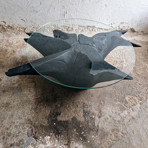 May include: A black wooden coffee table with a unique, tree-like design and a clear glass top.