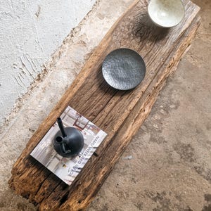 May include: A rustic wooden coffee table with a natural wood finish. The table has a rough, weathered surface and is decorated with two small bowls and a magazine. The magazine is titled "NAU INTERIOR IDEAS".