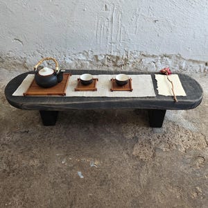 以下が含まれることがあります： 黒い持ち手と「But First, Coffee」の文字が黒い太字で書かれた白いセラミックマグ。マグカップは木製の表面に置かれています。マグカップの高さは約10cmです。
