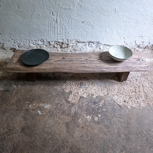 May include: A wooden serving tray with a dark green plate and a white bowl. The tray has a natural wood grain finish and is supported by two small legs. The background is a textured white wall. The tray is approximately 60 cm long.