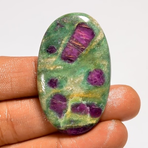 May include: Oval-shaped gemstone with a green base and vibrant magenta inclusions. The stone has a polished surface, showcasing a mix of colors and textures. The gemstone is held by a hand.