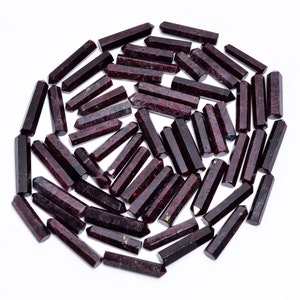 Op de afbeelding: Een verzameling van ongeveer 50 donkerrode edelsteenpunten, ook bekend als rode granaatpunten, gerangschikt in een cirkelvormige opstelling op een witte achtergrond.