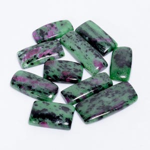 May include: A collection of ten green, black, and pink gemstone cabochons. The stones are rectangular and have a mottled appearance.