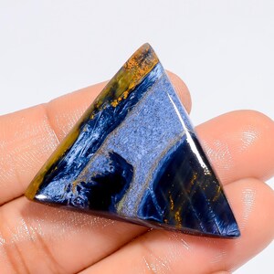 May include: A triangular cabochon of blue tiger's eye gemstone with gold and white streaks. The gemstone has a smooth, polished surface.