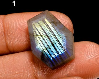May include: A dark gray, iridescent labradorite gemstone with a faceted, elongated shape. The stone displays a rainbow of colors, including blue, green, and gold.