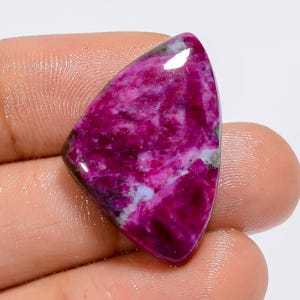 May include: A triangular cabochon gemstone with a pink and white pattern. The gemstone has a smooth, polished surface and is a vibrant shade of pink.