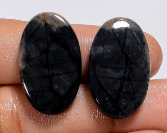 May include: Two oval-shaped black and gray gemstone cabochons with a marbled pattern. The cabochons are smooth and polished.