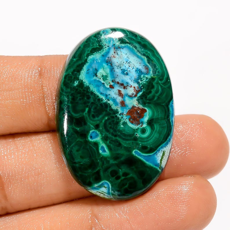 Puede incluir: Gema ovalada con una vibrante mezcla de colores. La piedra presenta una base de verde oscuro, con remolinos de patrones verdes m&aacute;s claros. Un &aacute;rea central muestra una llamativa mezcla de azul y turquesa, con toques de marr&oacute;n.