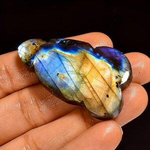 Peut inclure: Une pierre précieuse de labradorite polie de forme organique unique. La pierre présente un jeu de couleurs vibrant, avec des reflets bleus, jaunes et violets. La surface présente des motifs et des textures naturels visibles.