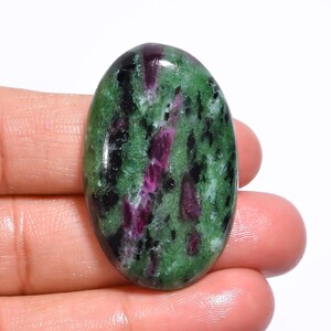 Puede incluir: Cabujón ovalado de piedra preciosa verde, rosa y negra. La piedra tiene un patrón moteado con vetas rosas y negras.