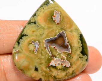 May include: A green, brown, and white agate cabochon with a teardrop shape. The stone has a unique pattern of swirls and circles.