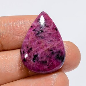 Può includere: Un cabochon di pietra preziosa rosa e nera tagliato a goccia. La pietra preziosa presenta un motivo screziato ed è lucidata a lucentezza elevata.