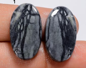 May include: Two oval-shaped, gray and black, natural stone cabochons. The stones have a marbled pattern with white, gray, and black swirls.
