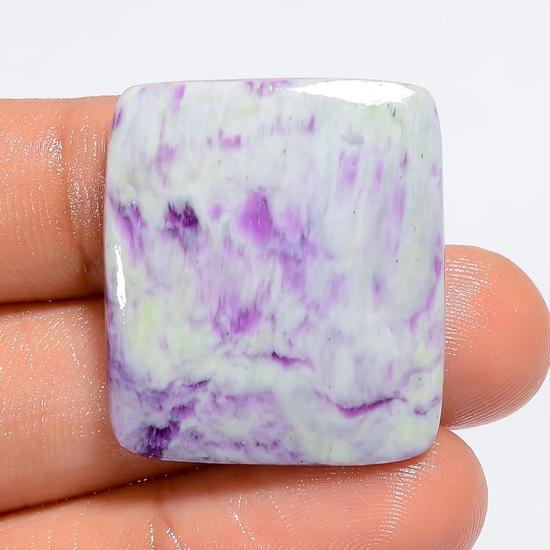Puede incluir: Un cabuj&oacute;n cuadrado de piedra preciosa de sugilita p&uacute;rpura y blanca. La piedra tiene un patr&oacute;n de remolino de p&uacute;rpura y blanco.