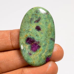 Può includere: Gemma ovale con una base verde macchiata e inclusioni rosso intenso. La superficie lucidata riflette la luce, evidenziando i motivi e i colori naturali della pietra. Ideale per la creazione di gioielli.
