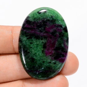 May include: Oval-shaped green, pink, and black gemstone cabochon. The gemstone has a smooth, polished surface.