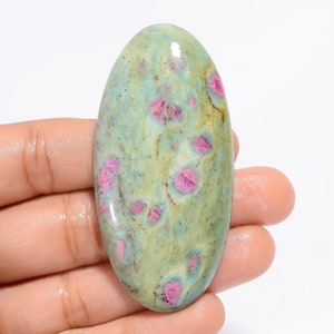 Op de afbeelding: Ovale cabochon edelsteen met een groene basis en roze robijn insluitsels. De steen heeft een gemarmerd uiterlijk met een mix van licht- en donkergroene tinten.