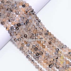 Puede incluir: Una hebra de cuentas redondas de ágata blanca con patrones dendríticos negros. Las cuentas tienen aproximadamente 6 mm de diámetro y están enhebradas en un cordón elástico transparente.