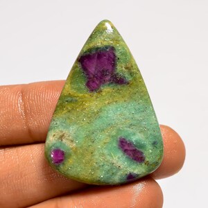 Puede incluir: Una piedra preciosa pulida con forma triangular. La piedra presenta un color base verde y amarillo con inclusiones magenta vibrantes. La superficie tiene un aspecto moteado, lo que aumenta su belleza natural. Ideal para la creación de joyas.