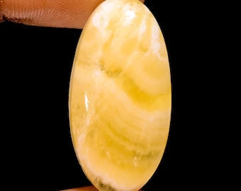May include: A yellow oval cabochon gemstone with white and yellow swirls. The gemstone is smooth and polished.
