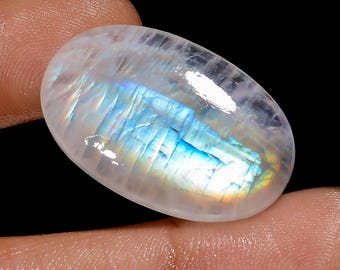 Può includere: Un cabochon ovale di pietra di luna bianca con riflessi iridescenti blu e verdi.