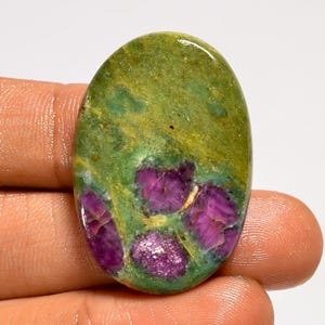 May include: Oval-shaped gemstone with a mix of colors. The top portion is a mottled green, transitioning to a vibrant magenta with hints of white and yellow. The stone has a polished surface, showcasing its natural patterns and textures.