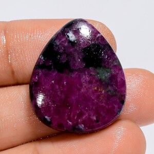 Peut inclure: Une pierre précieuse en cabochon en forme de larme avec une couleur violet foncé et noire. La pierre a un aspect marbré avec un mélange de teintes foncées et claires.