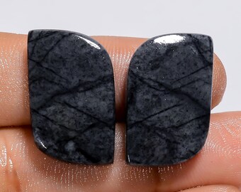 Könnte beinhalten: Zwei graue und schwarze Edelstein-Cabochons mit einem marmorierten Muster. Die Cabochons sind tropfenförmig mit einer abgerundeten Oberseite und einer spitzen Unterseite.