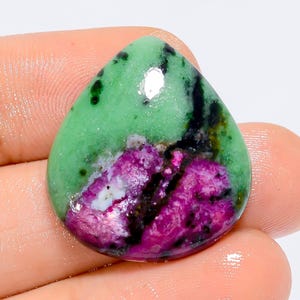 Può includere: Un cabochon di pietra preziosa verde e rosa con inclusioni nere. La pietra preziosa è tagliata a forma di lacrima.
