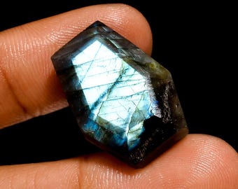 May include: A faceted, dark blue labradorite gemstone with iridescent flashes of color. The gemstone is cut in a hexagonal shape and has a smooth, polished surface.