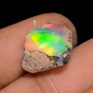 Op de afbeelding: Een ruwe, iriserende opaal edelsteen met een mix van groene, roze en gele kleuren. De opaal is gezet in een natuurlijke matrix.