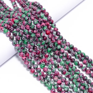 Peut inclure: Un brin de perles de pierres précieuses vertes et roses. Les perles sont rondes et ont un aspect moucheté.