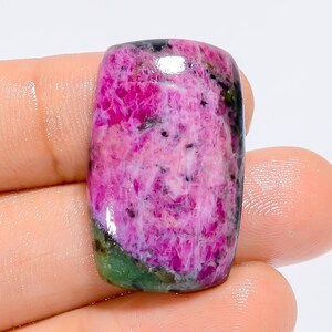 Può includere: Un cabochon di pietra preziosa rosa e verde con una superficie liscia e lucida. La pietra presenta un motivo a spirale di rosa, bianco e verde.