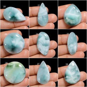 May include: Nine different cabochon gemstones, each with a unique pattern of blue, green, and white. The gemstones are all oval or teardrop shaped and are arranged in a grid.