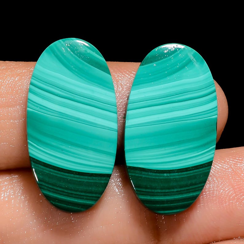 May include: Two oval-shaped green and white malachite cabochons with a swirling pattern. The cabochons are smooth and polished.